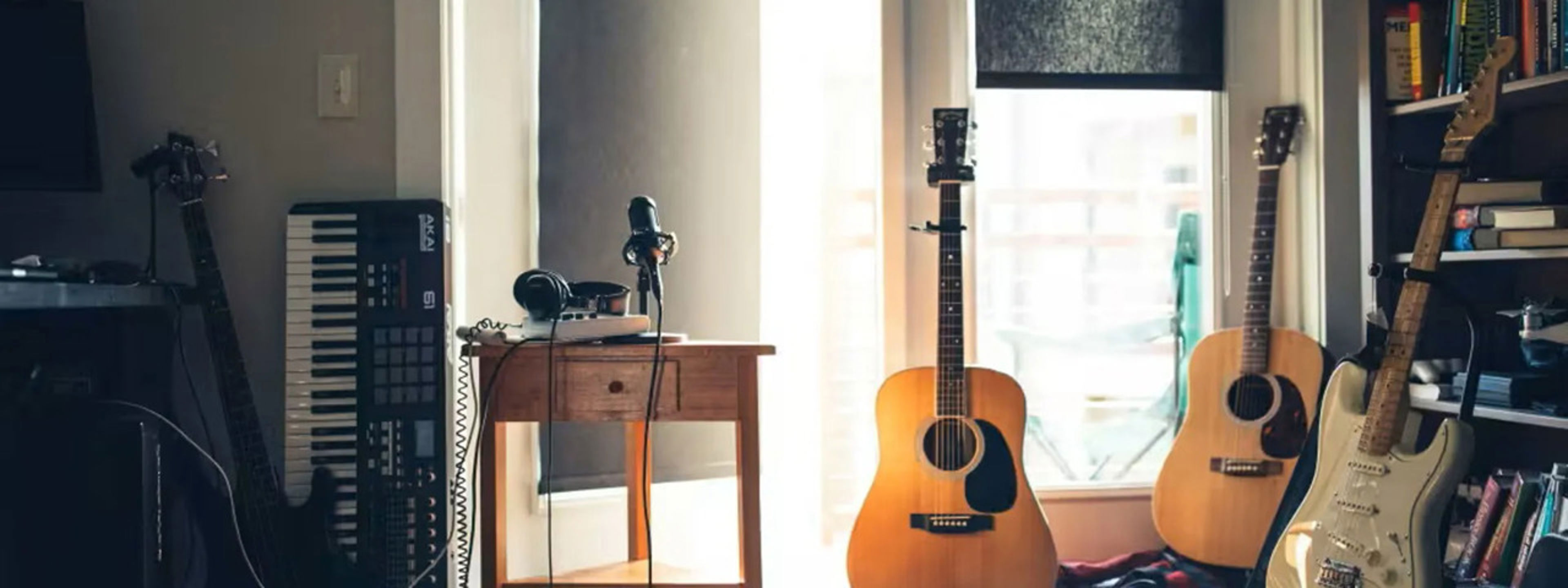 Musikkrom med oppsett av forskjellige instrumenter som gitar og keyboard, samt også headet og mikrofon på et bord. På høgre side er det en bokhylle med bøker