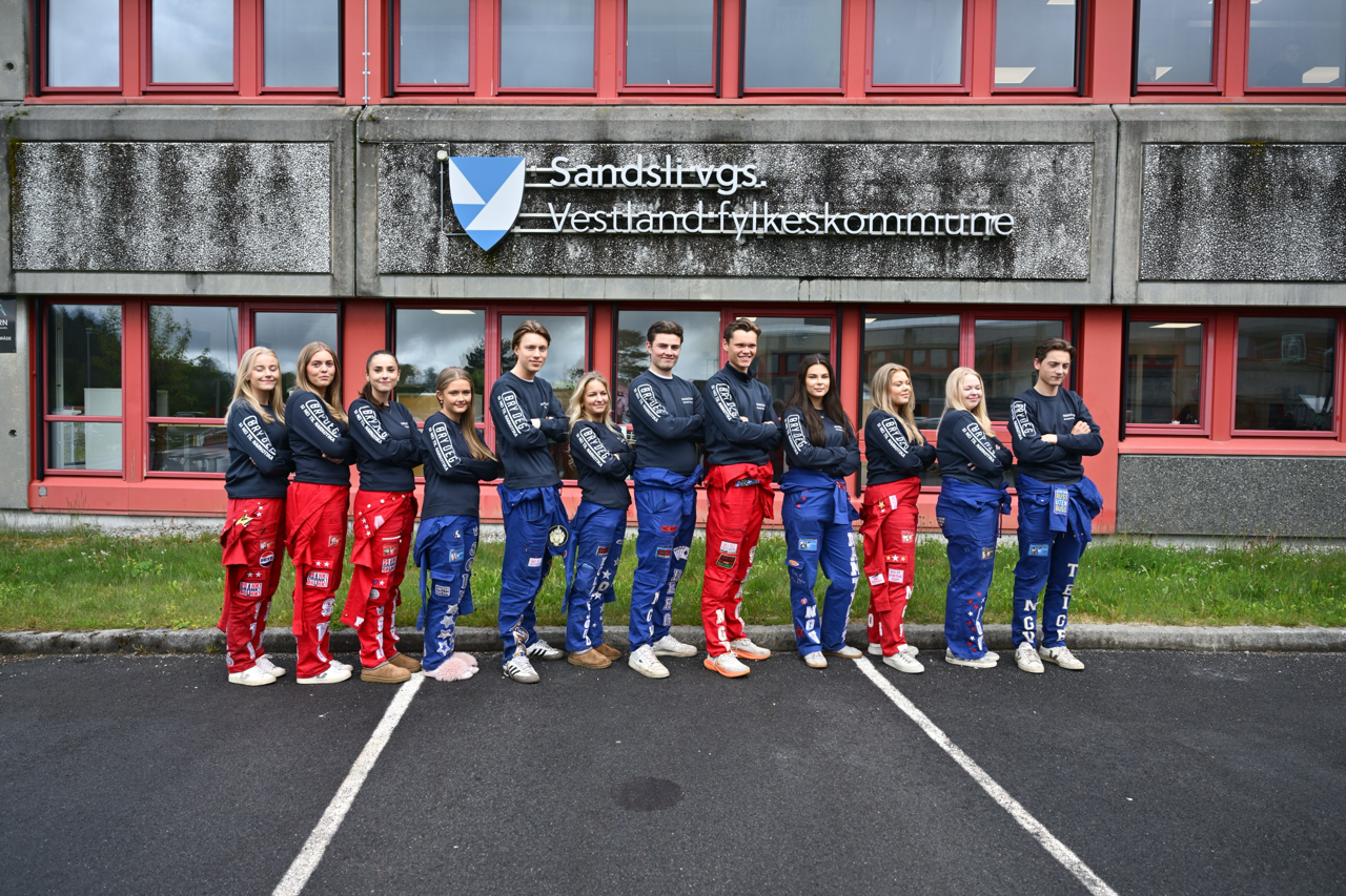 Russen på Nordahl Grieg og Sandsli som står foran logoen til Sandsli vgs utenfor skolen på en rekke