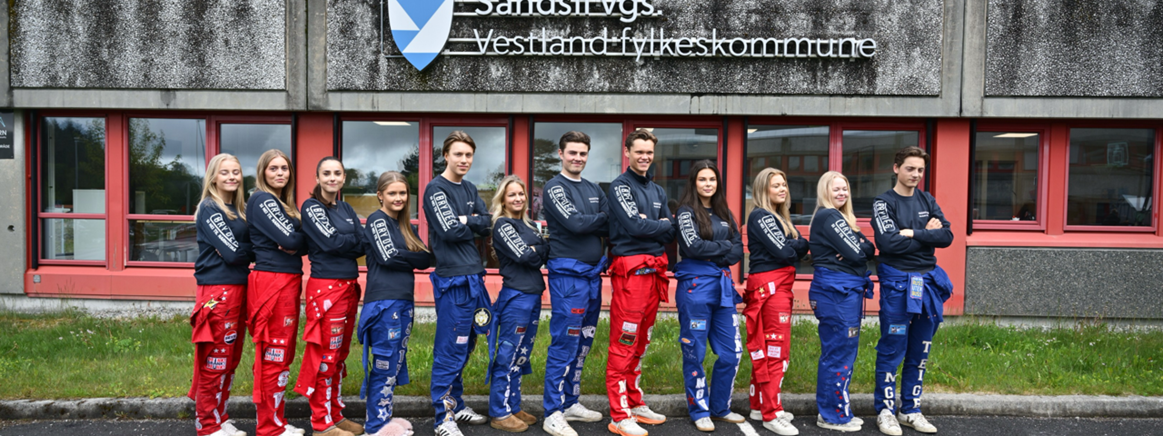 Russen på Nordahl Grieg og Sandsli som står foran logoen til Sandsli vgs utenfor skolen på en rekke