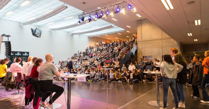 Politisk debatt i Skoletorget. Representanter for politiske partier sitter foran fullsatt sal av elever.