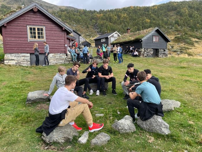 vg1 elever sitter i ring og prater sammen. I bakrunnen sæterhus og flere elever.